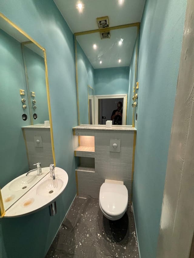 Small bathroom being painted teal, with a new mirror cabinet fitted and protective tape still up