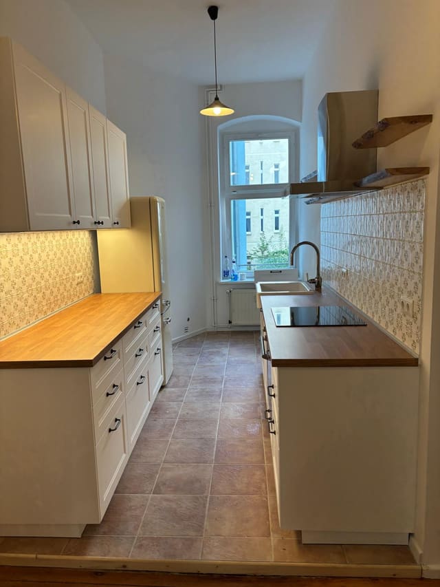 White shaker kitchen with patterned tile splashback and oak worktop, fitted in a Berlin Altbau flat