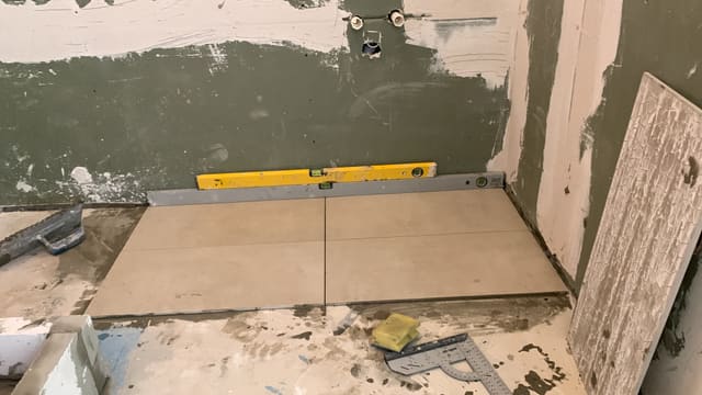 Small tiled floor area being laid with a spirit level checking the line
