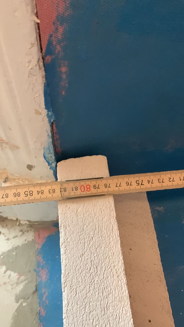 Blue mosaic wall tiling in progress with a tape measure checking alignment