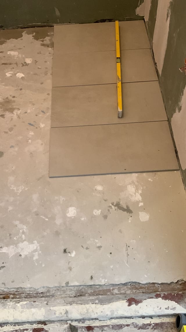 Cream floor tiles being laid over exposed subfloor
